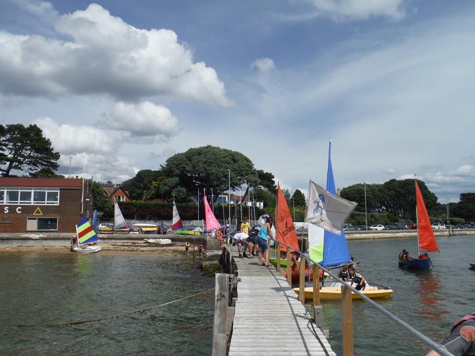 Members on the club pontoon with dinghies rigged on the beach